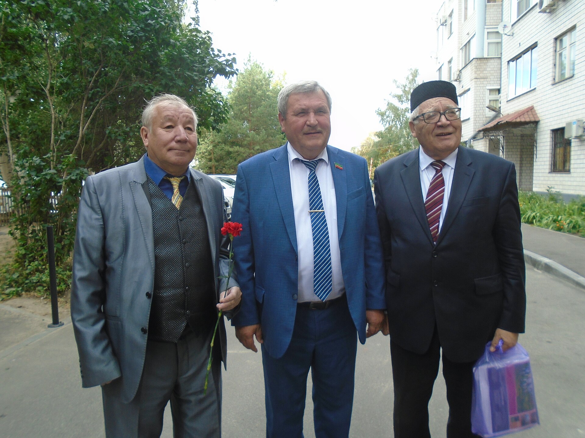 Three men in suits stand on a street with flowers and gifts, representing the cultural richness of Urdu poetry.